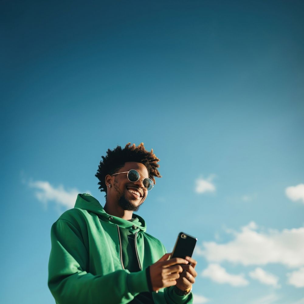 photo of black man wearing green tone outfit using smartphone. 