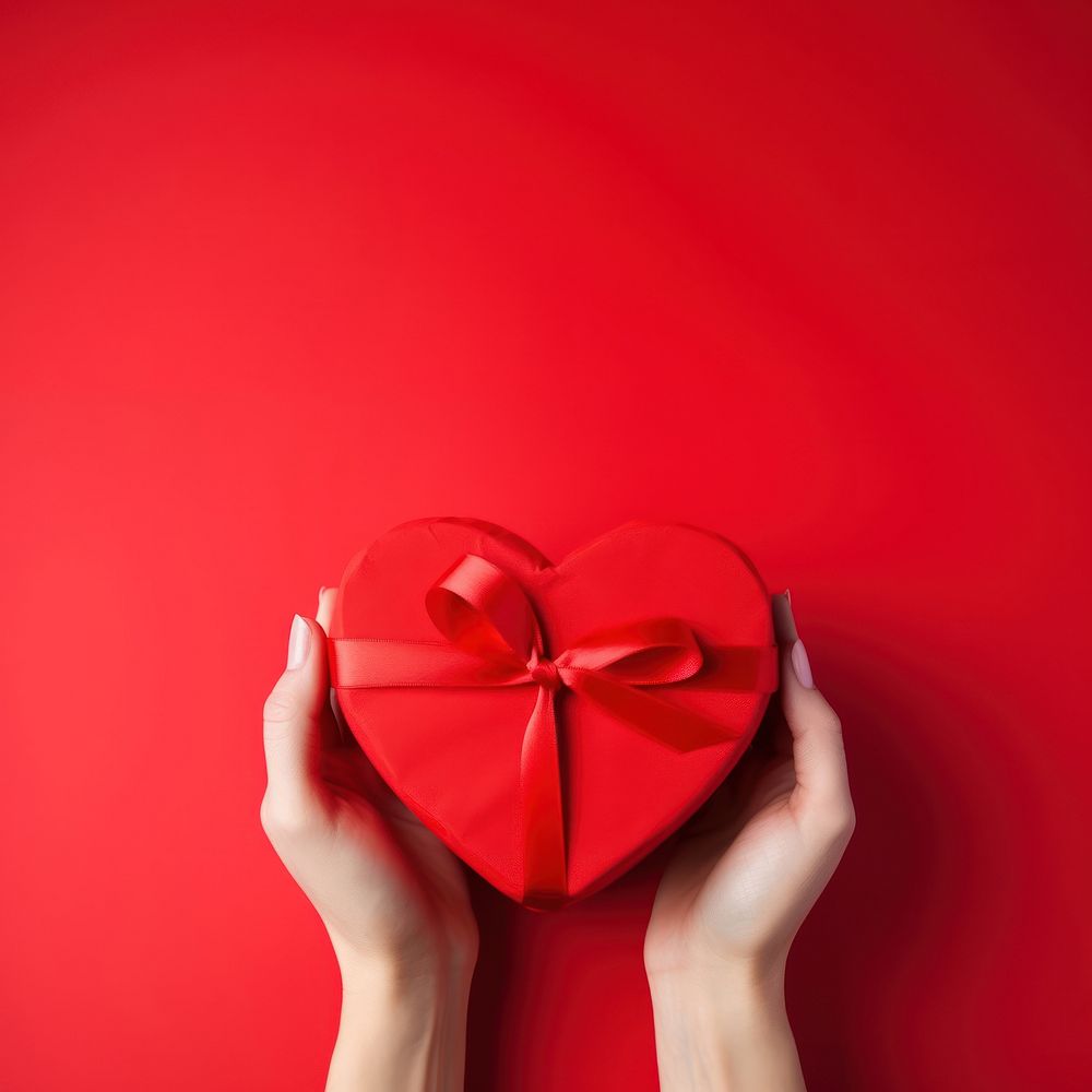 A photo of hands of woman holding a nice shape valentines present on red background.  