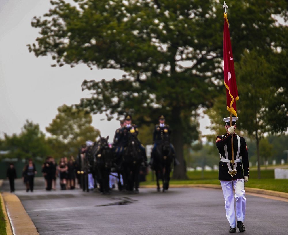 A Marine carries a general officer flag during the procession for a full honors funeral at Arlington National Cemetery…