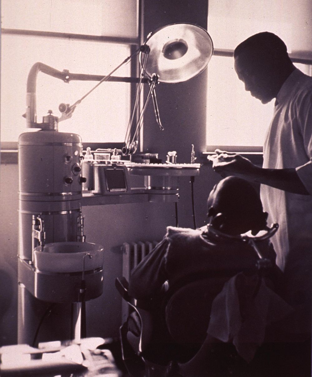 Dental office visit. Abstract: Interior view of a dental office with an African American patient sitting in the dental chair…
