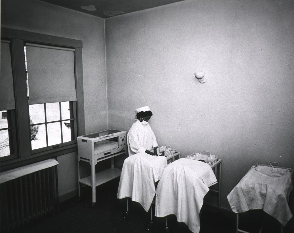 Indian Hospital. An African American nurse is at the bedside of a newborn in the nursery. Original public domain image from…