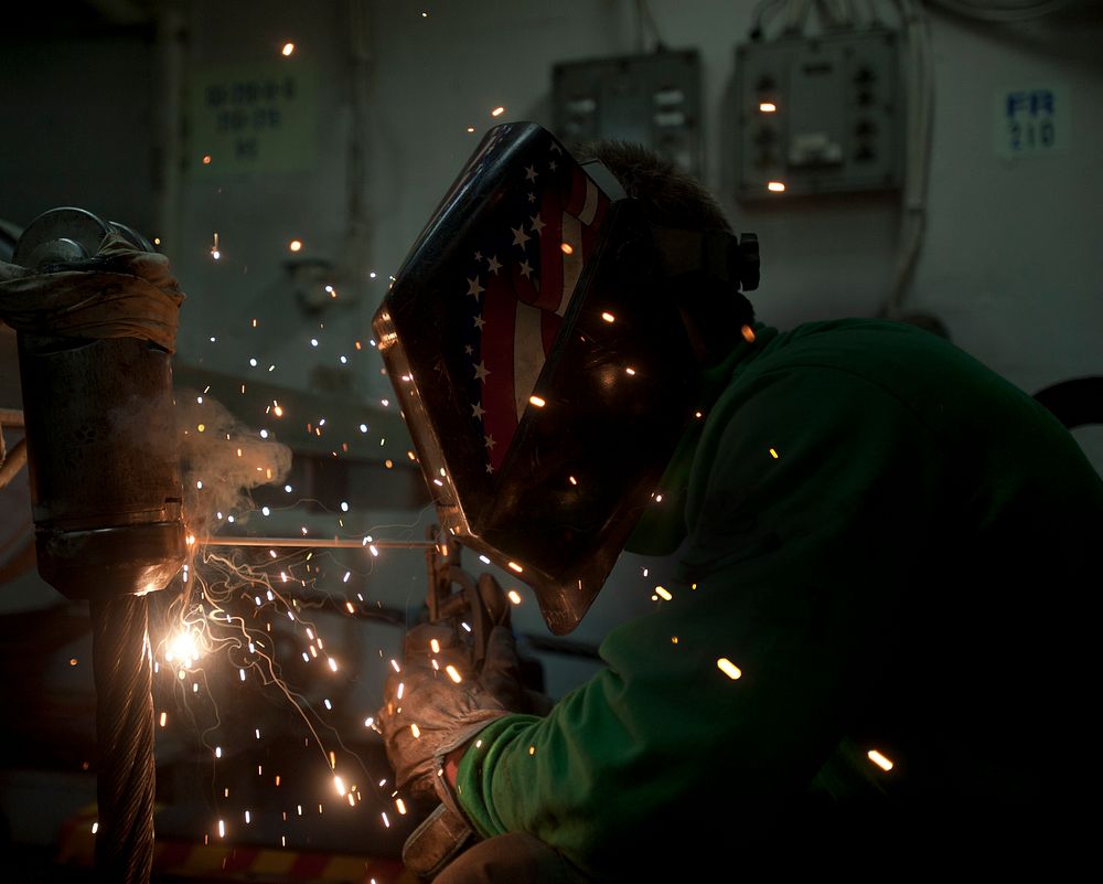 U.S. Navy Aviation Boatswains Mate Equipment 3rd Class Devin McMaster welds an anchor terminal on an arresting gear cable…
