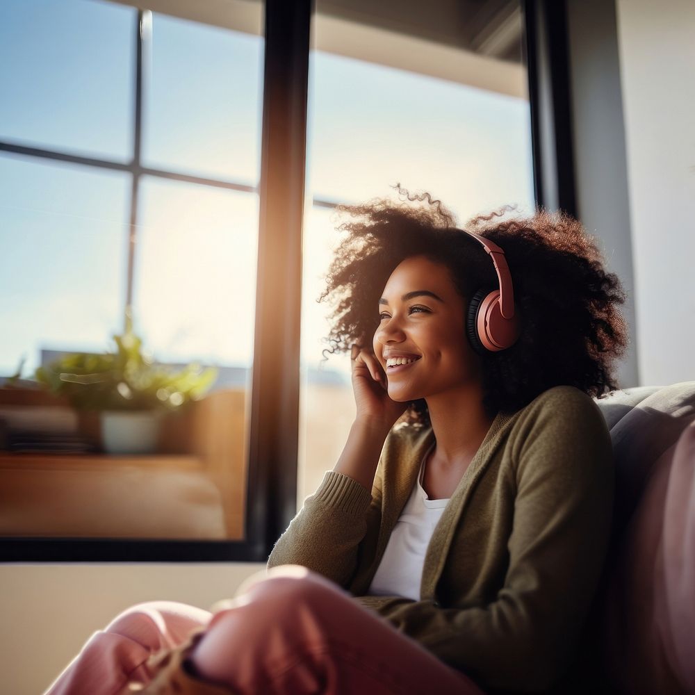 photo of A black woman sitting on a couch happy with wearing headphones in a minimal living room. 