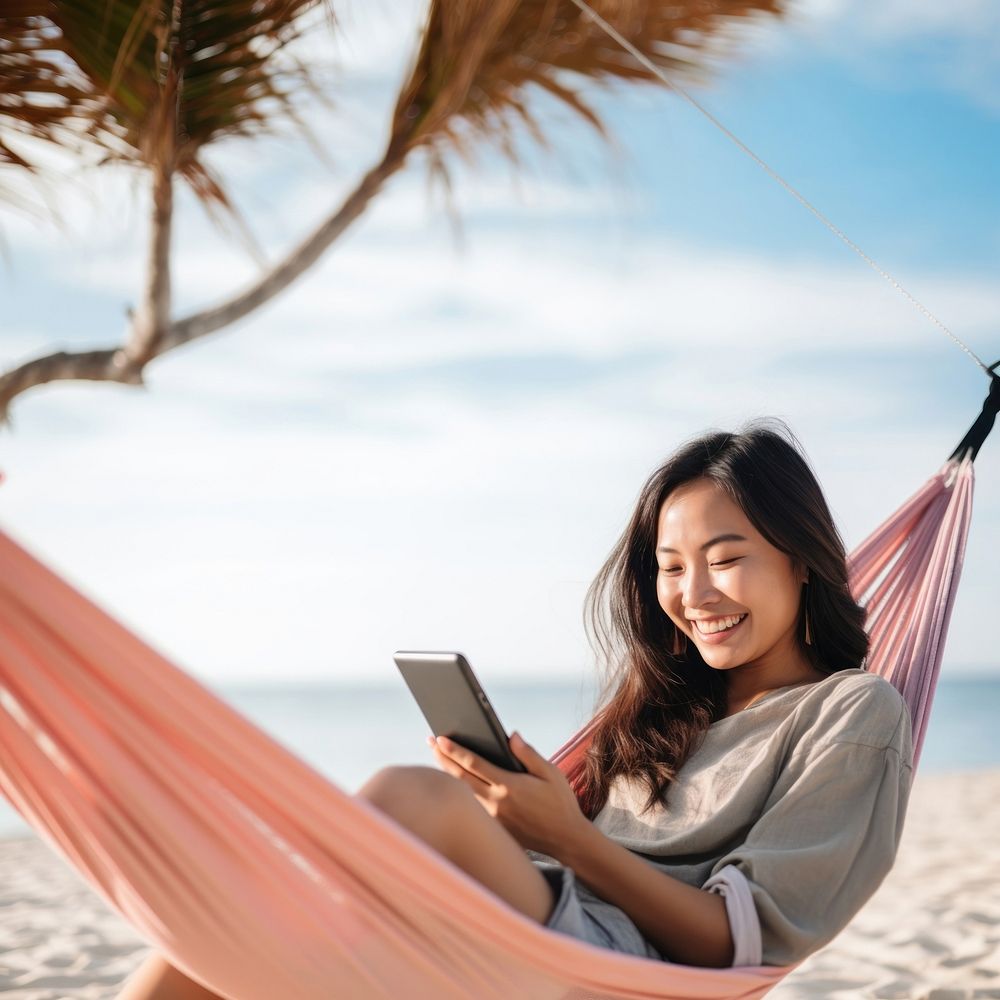 Happy traveler asian woman using mobile phone and relax in hammock on beach. 