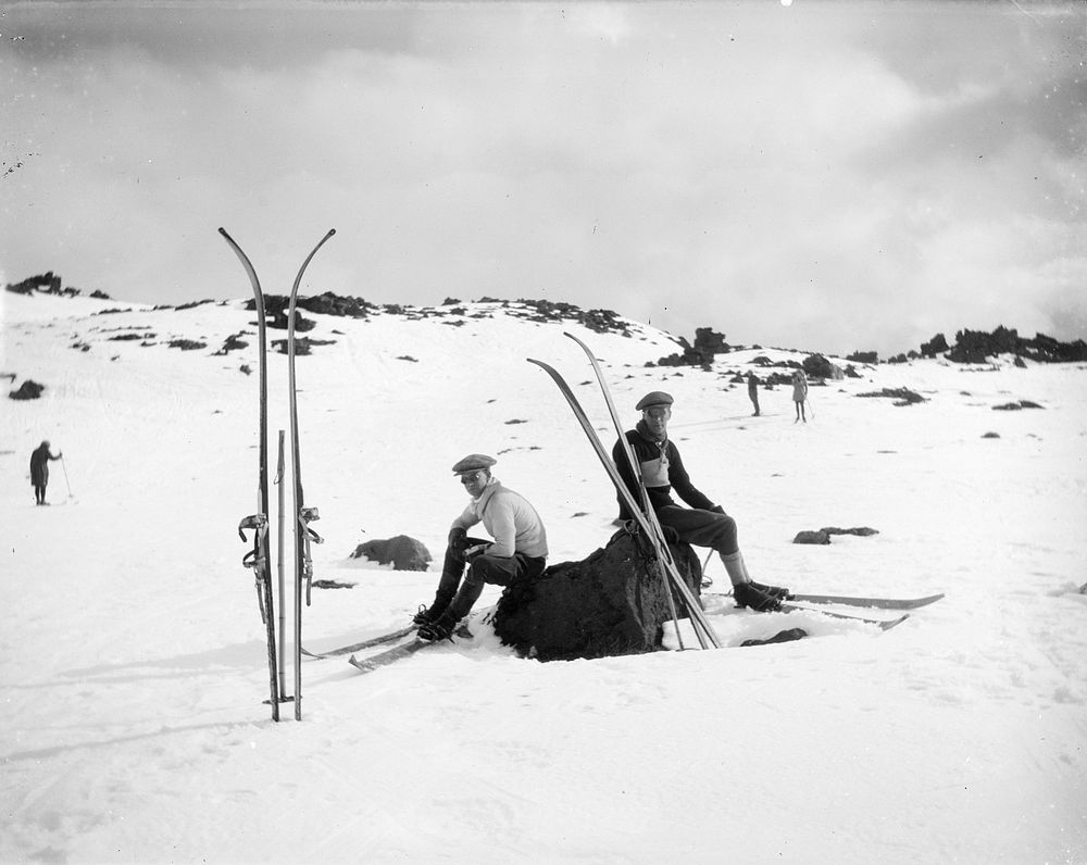 Two men resting on rocks with skis nearby by Leslie Adkin.
