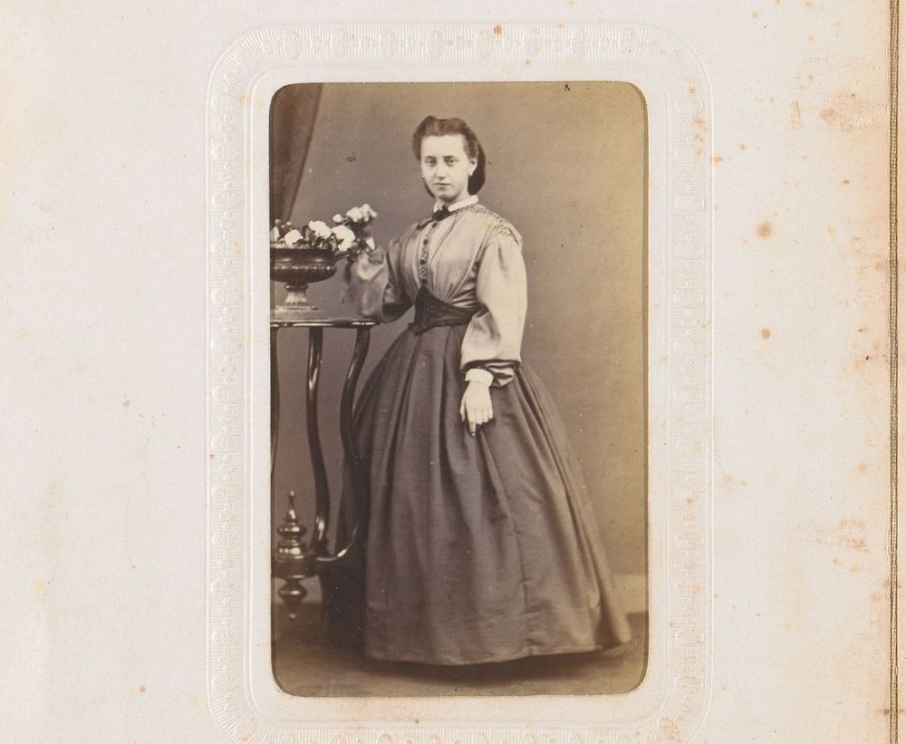 Portret van een vrouw, staand bij een hoge tafel met vaas met bloemen (1860 - 1900) by anonymous