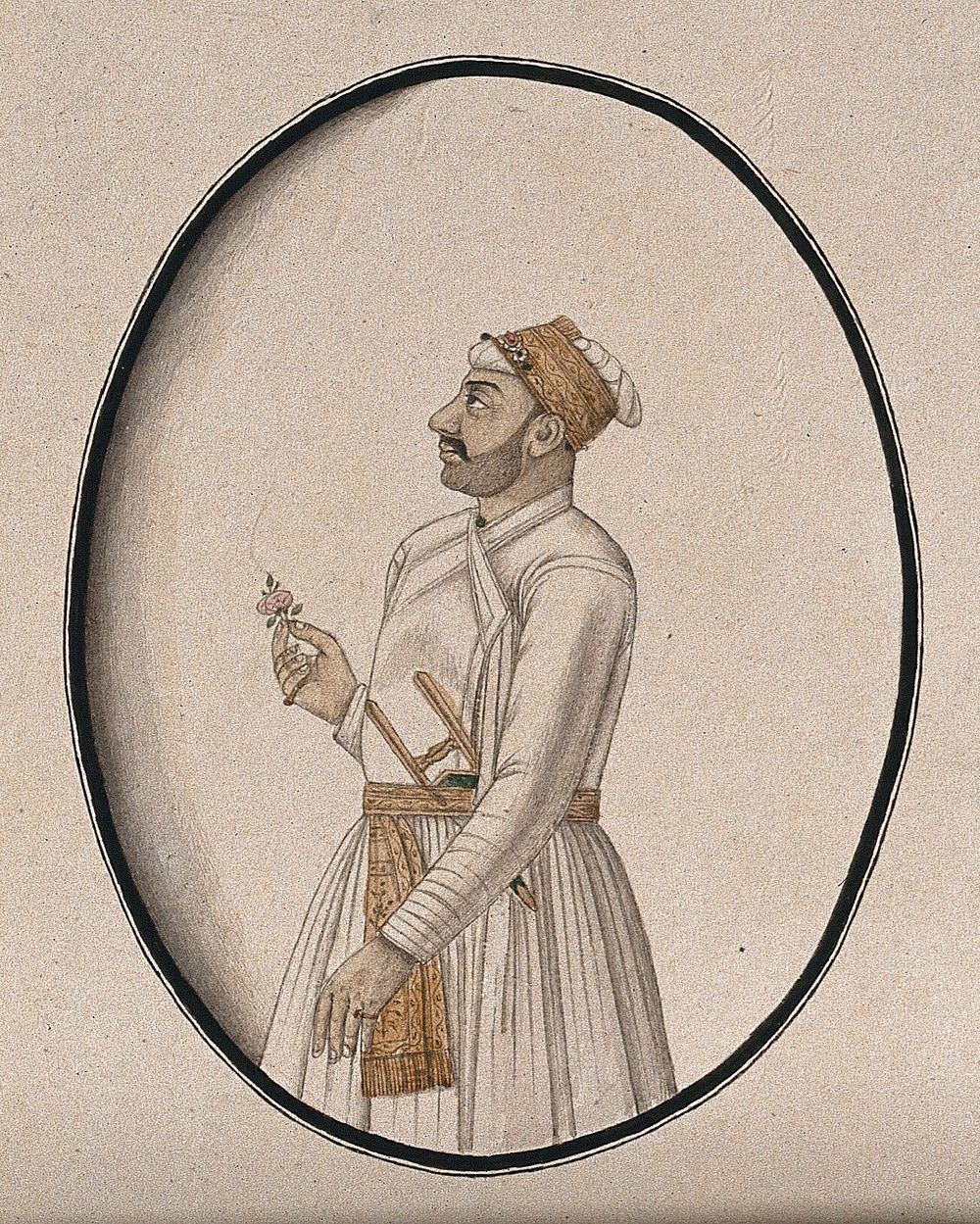 A Mughal courtier carrying a dagger and holding a flower. Watercolour drawing by an Indian artist.