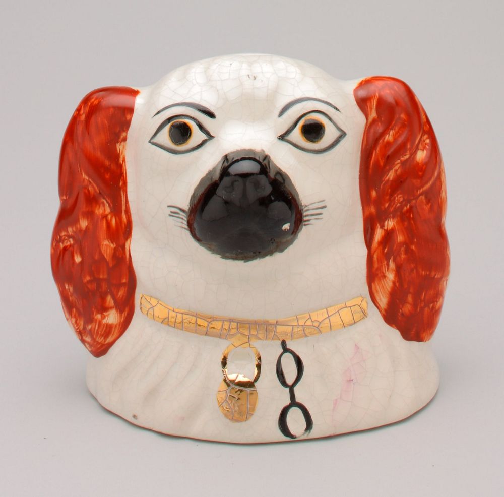 Staffordshire-style dog's head; black muzzle; red ears; gold collar with black chain; coin slot at top of head; shiny glaze…