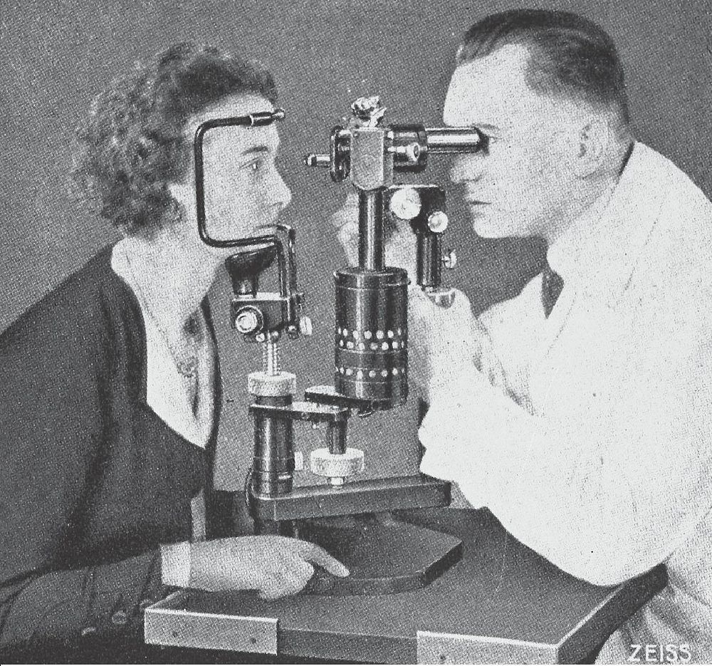 Eye examination with a Zeiss biomicroscopic apparatus. Black and white image of a young woman having her eyes examined by a…