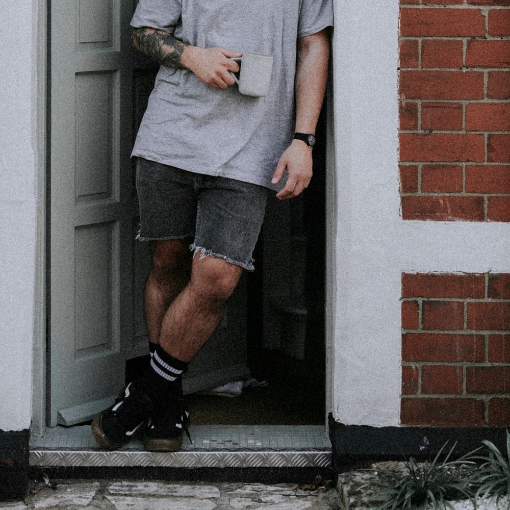 Man holding coffee mug, standing by his doorway