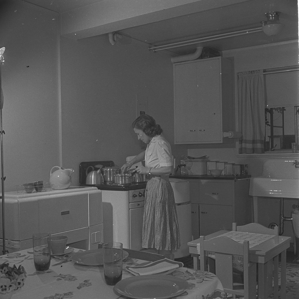 Greenbelt, Maryland. Federal housing project. Mrs. Leslie Atkins preparing dinner in her kitchen, one end of which is the…