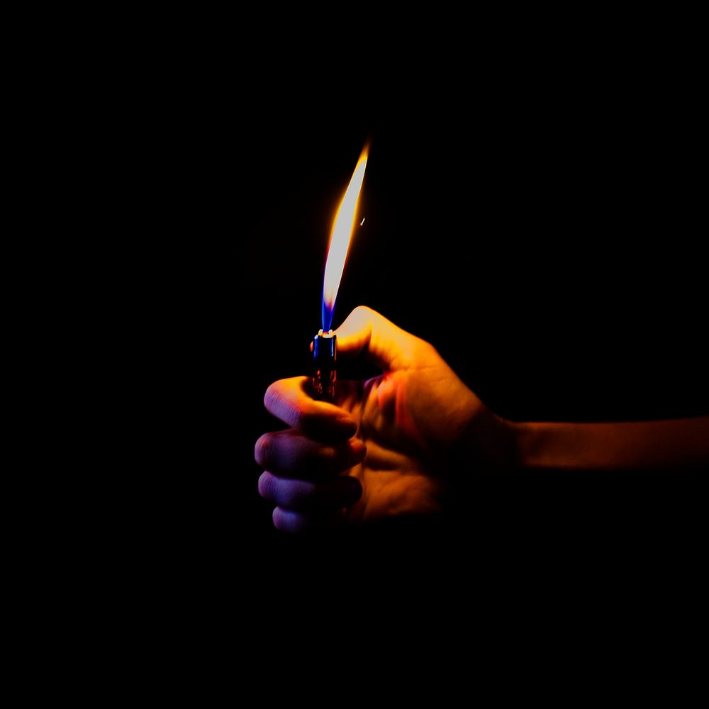 Hand holding a lit lighter in the dark