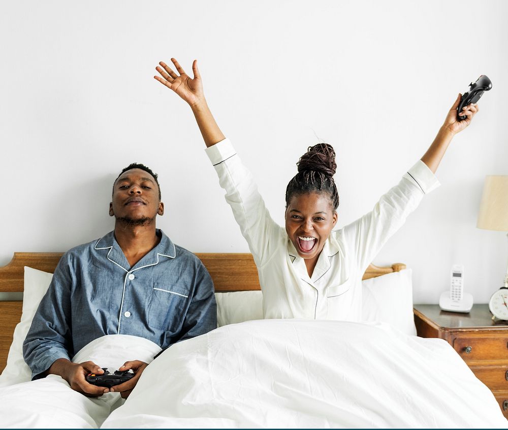 A happy couple playing video game in bed