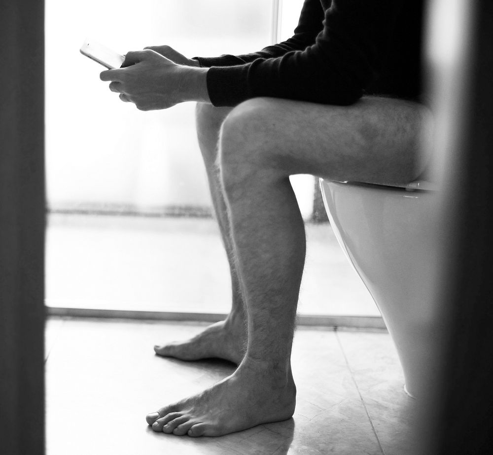 Man on the toilet seat using a smarphone