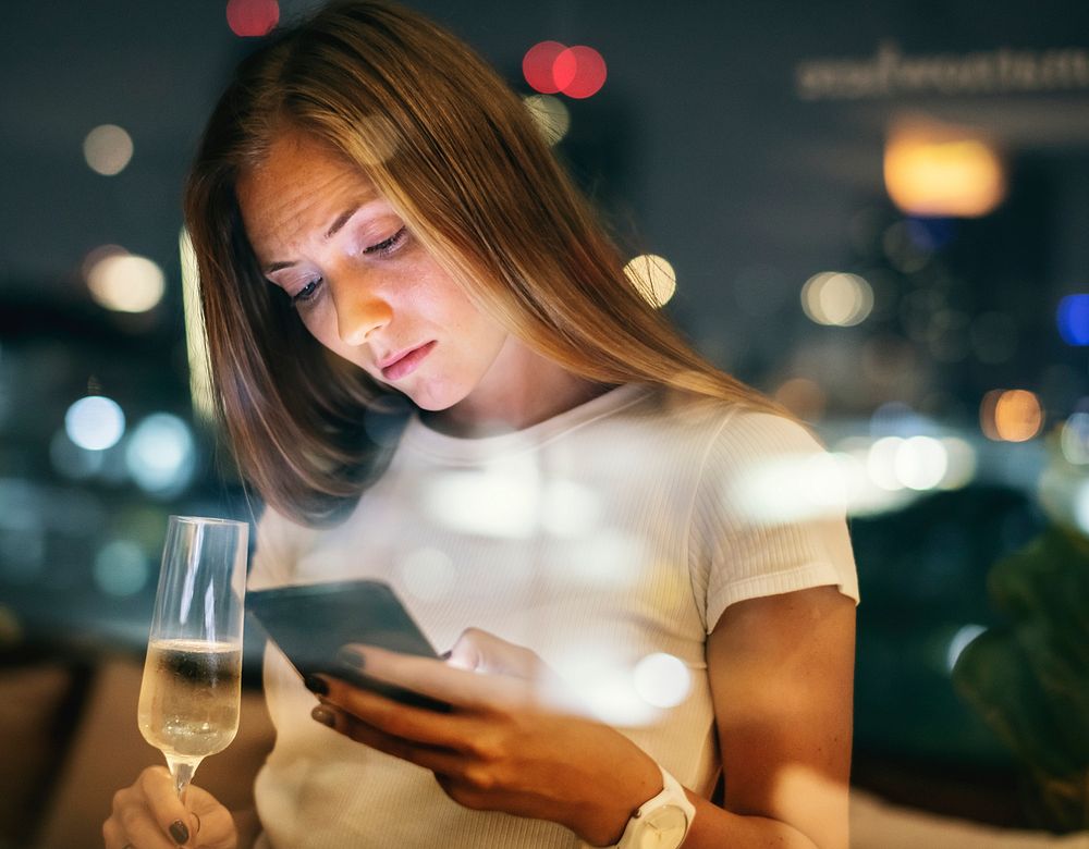 Serious young woman using a smartphone at a rooftop bar in the evening