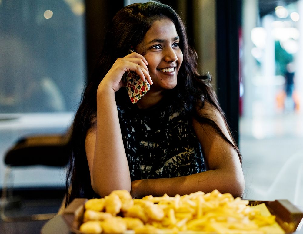 Close up of teenage girl talking on a phone eating french fries youth culture concept