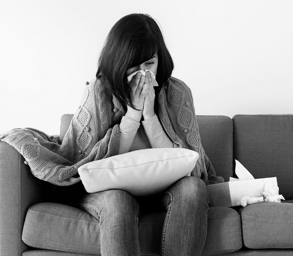 Sick woman sneezing on the sofa grayscale