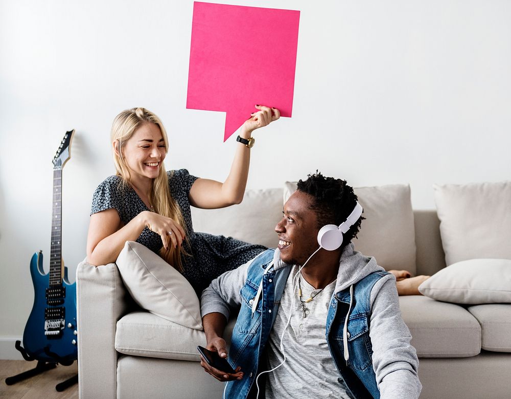 Interracial couple sharing music at home holding copyspace speech bubble