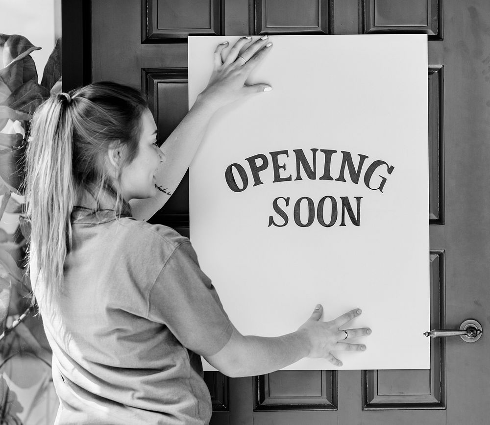 Woman putting on store opening soon sign