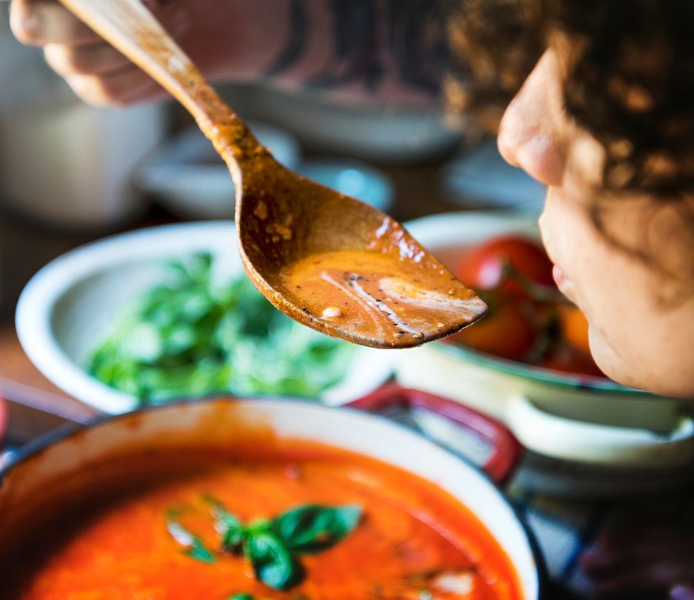 Woman tasting a tomato soup in the kitchen