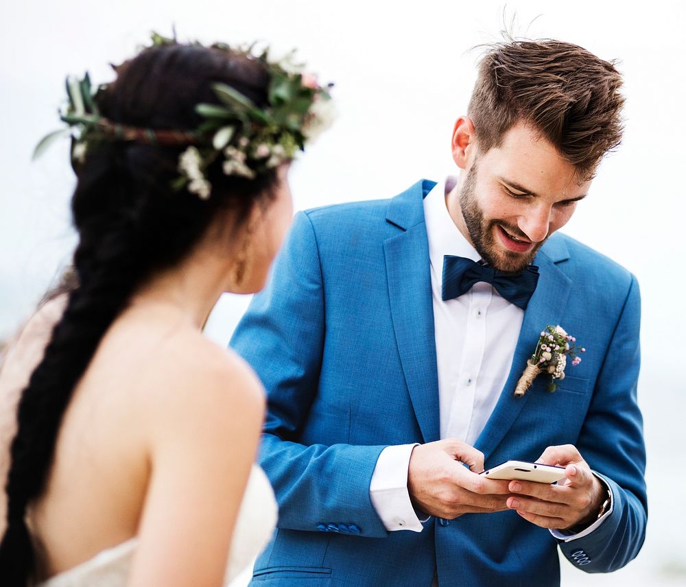 Groom checking his phone at beach wedding ceremony