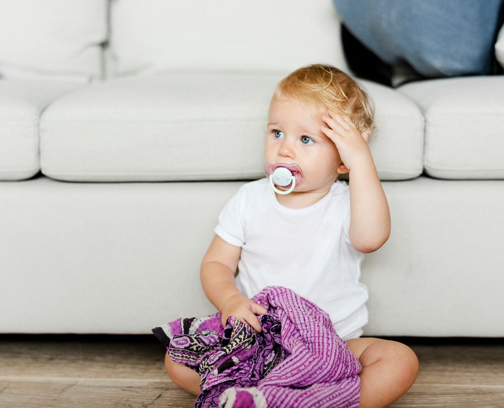 Baby with a pacifier and a blanket on the floor