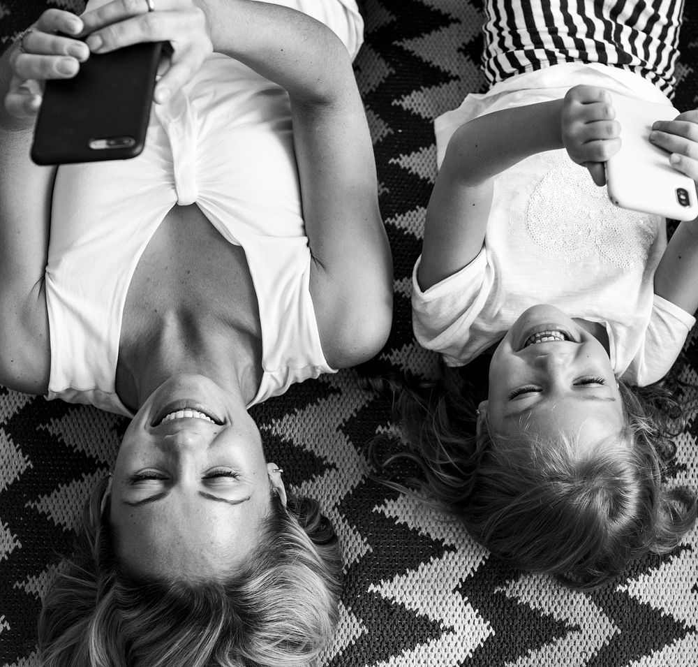 Mom and daughter lying on their backs using their phones