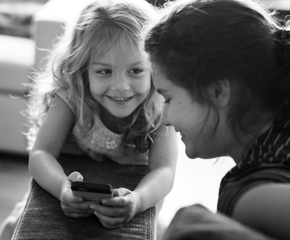 Little girl showing something from her phone to her big sister