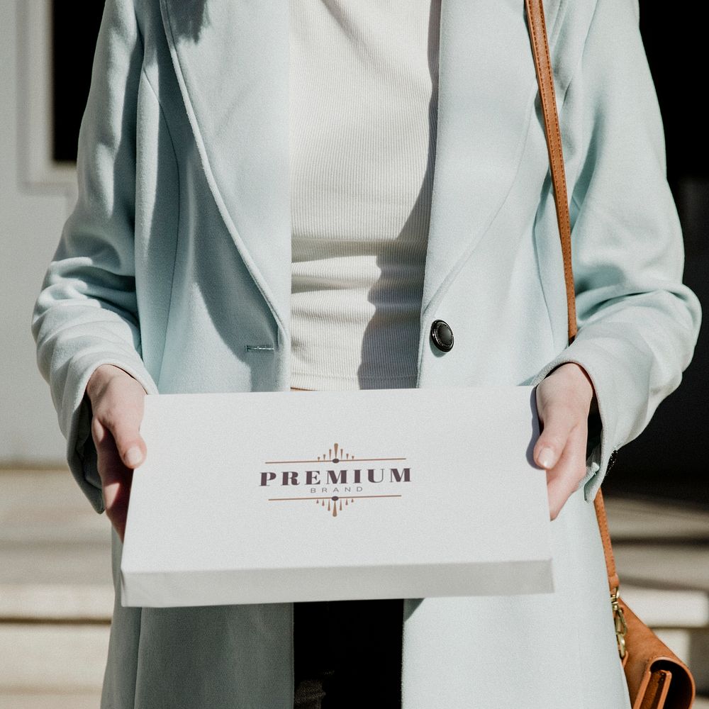 Woman in an overcoat carrying a white box in front of a building