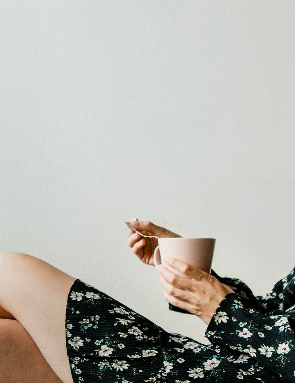 Woman sitting by a white wall with a cup of tea