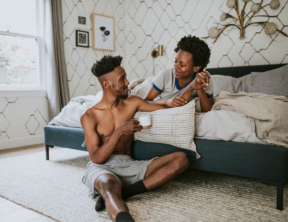 Happy black couple enjoying a conversation in bed while drinking coffee