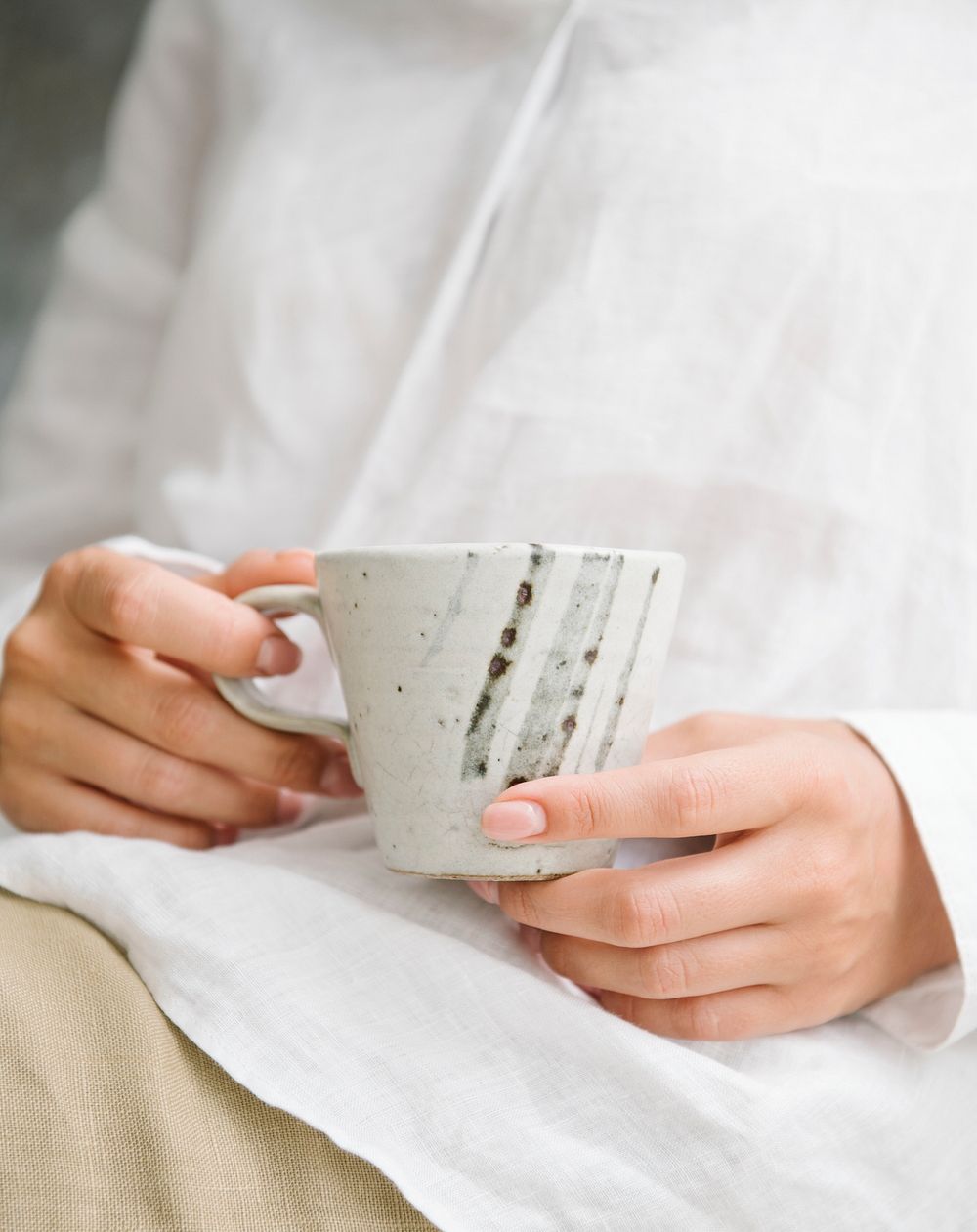 Woman in a white shirt holding a cup of coffee on her laps