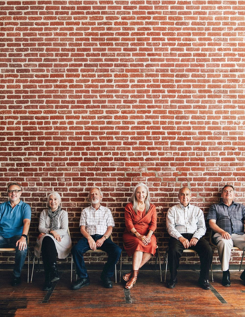 Diverse elderly people sitting in a row against a brick wall background