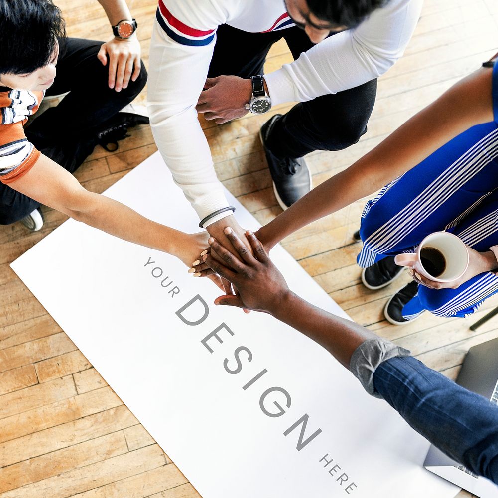 Diverse team stacking hands over a project plan mockup