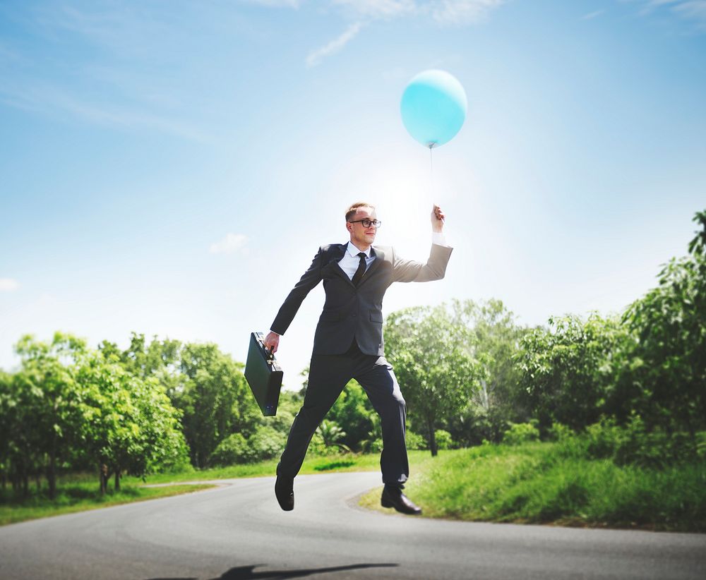 Playful businessman outdoors holding a helium balloon