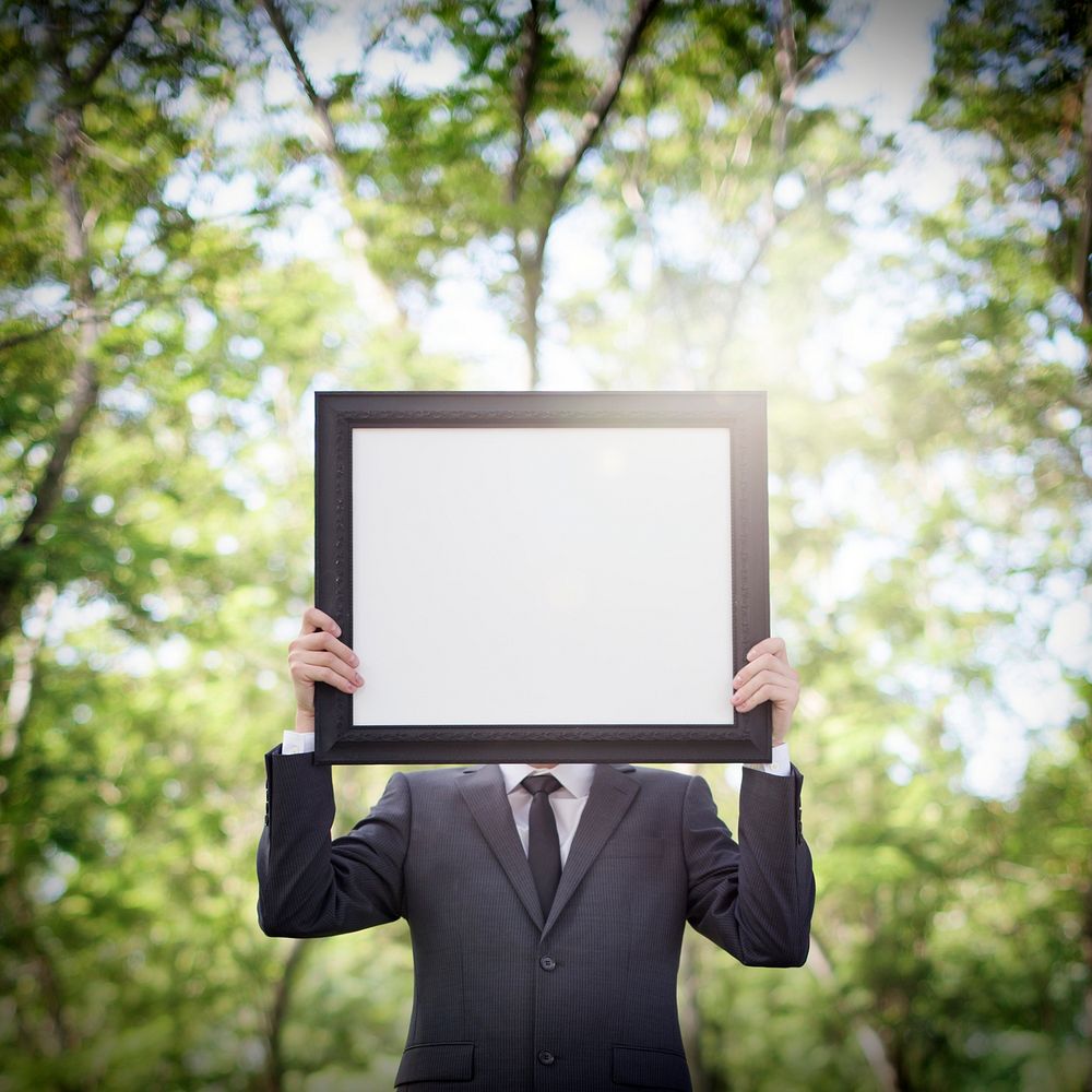 Businessman holding a blank frame in nature