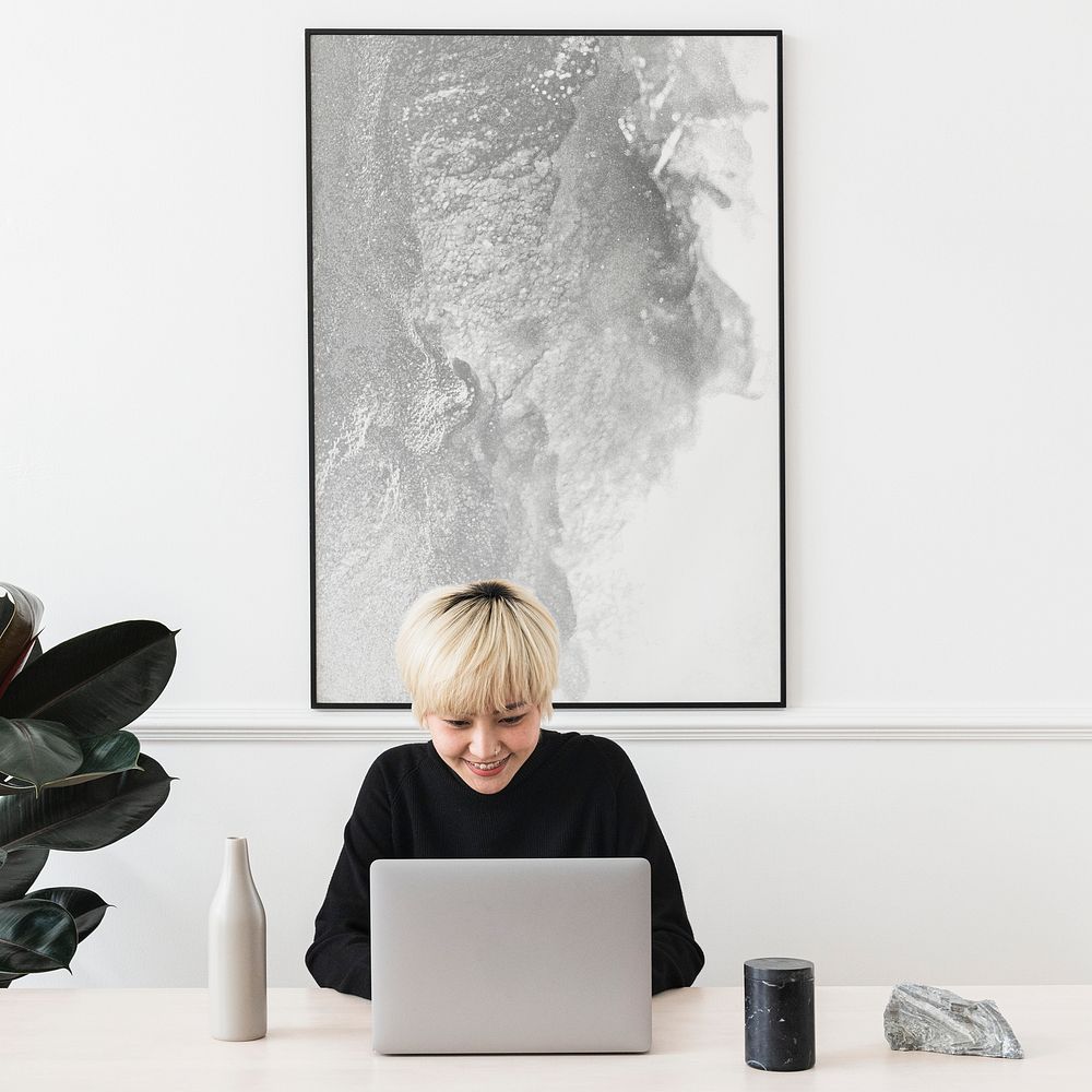 Woman working on her laptop with a frame hanging on a wall mockup
