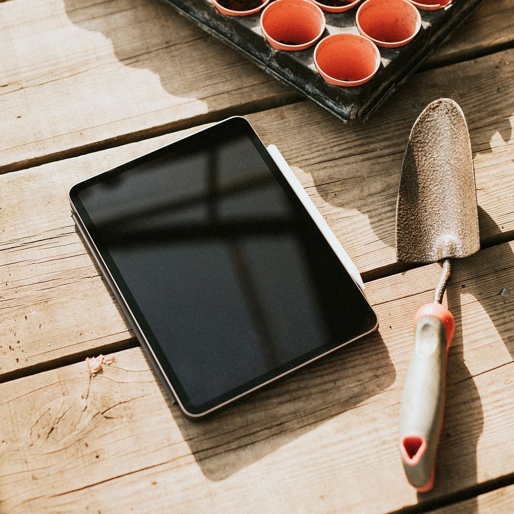 Psd black tablet screen mockup by a gardening trowel on a wooden table