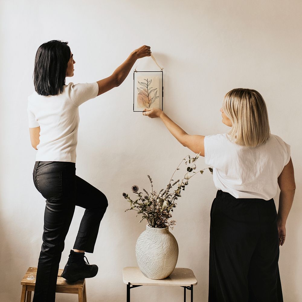 Women hanging frame on white wall