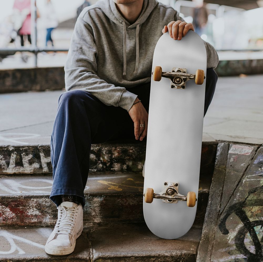 Man in gray hoodie sitting with white skateboard on steps