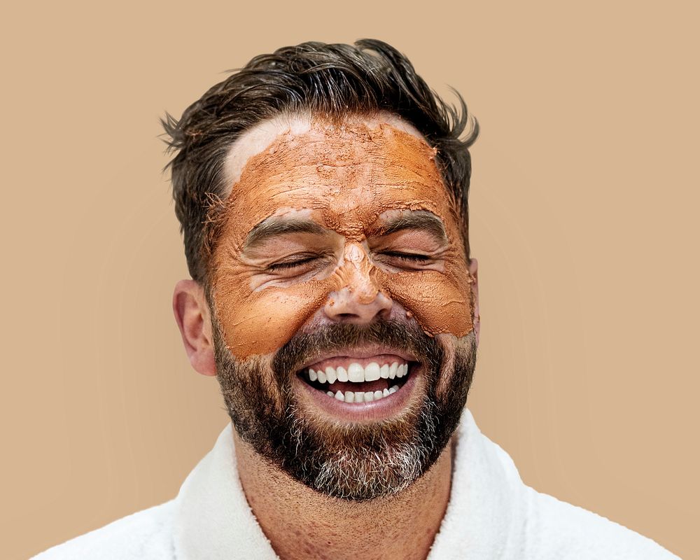 Laughing man in bathrobe with facial mask isolated on background