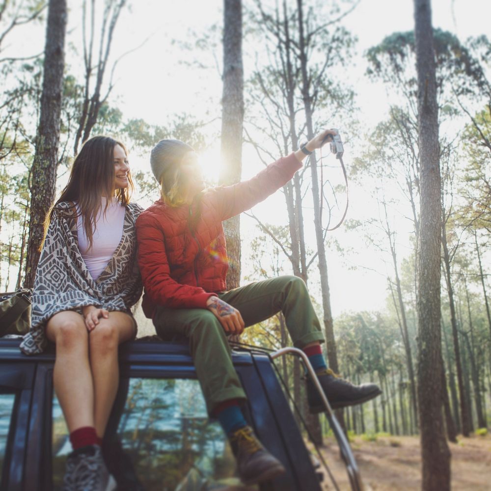 Couple sitting on top of a car in the forest
