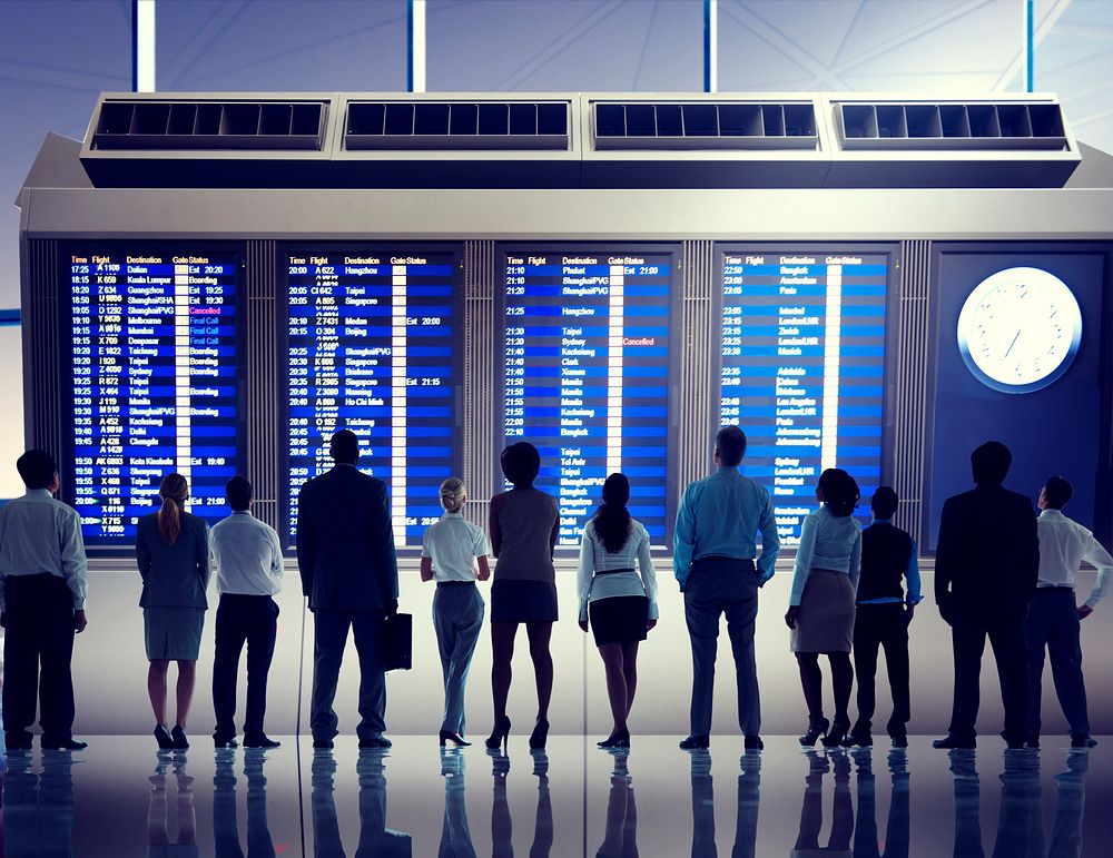 Silhouette of business people standing in a row in front of an airport timetable