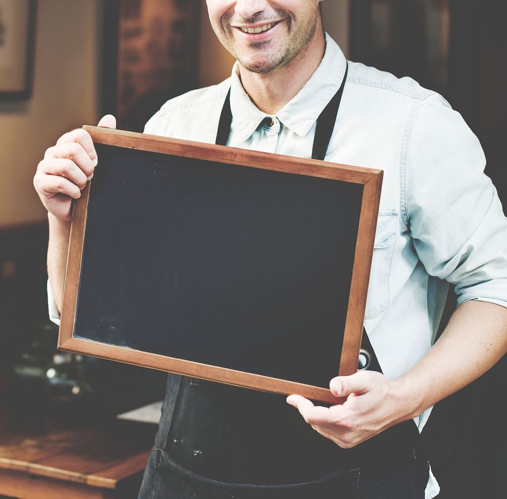 Happy man with an apron holding an empty blackboard