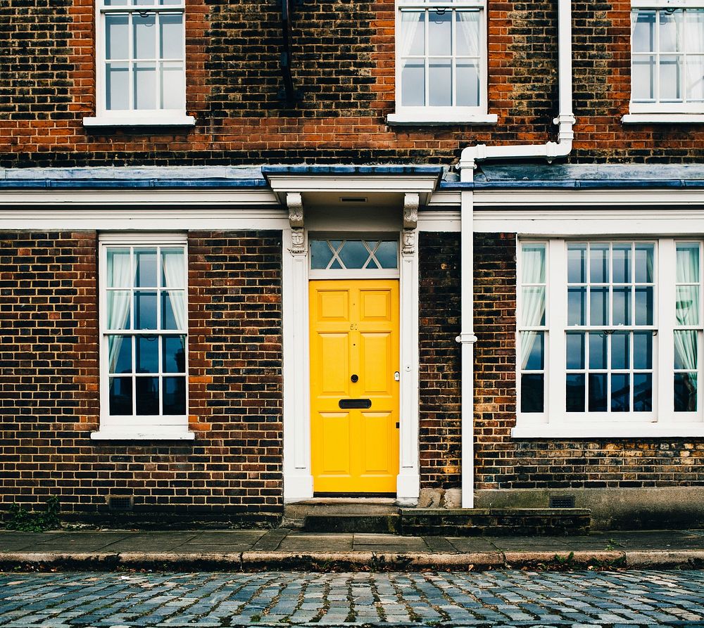 A bright yellow door in the center of the frame pops in an otherwise drearily colored image of a two-storey brick dwelling…