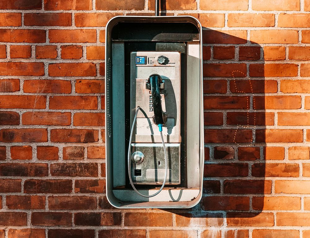 Photo of an old American-style payphone on a red brick wall, free public domain CC0 image.