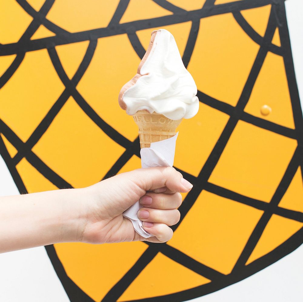 Hand holding soft serve ice cream in front of an ice cream truck, free public domain CC0 photo.