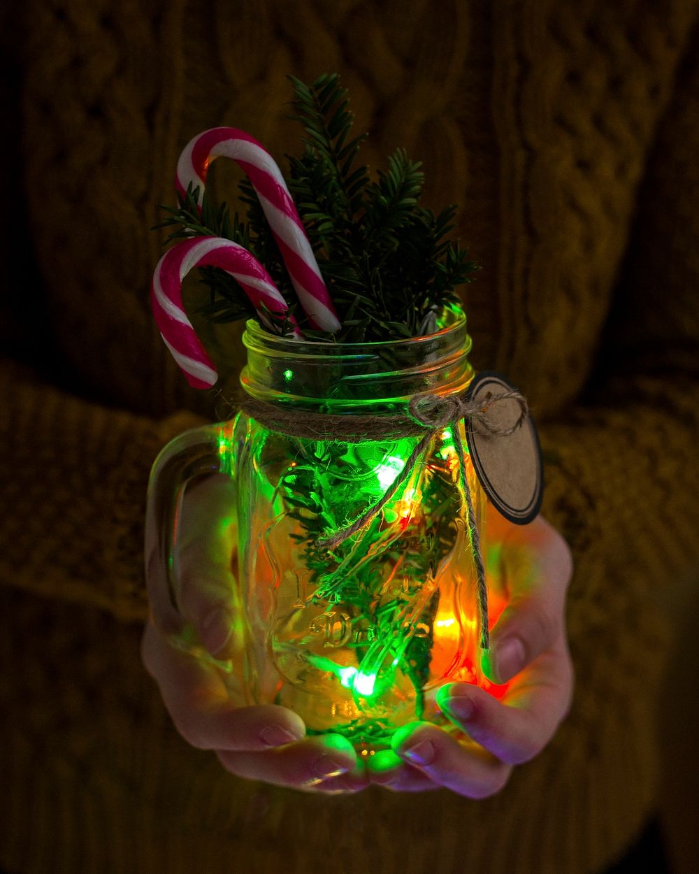 Close up of hands holding a mason jar with Christmas decorations and light