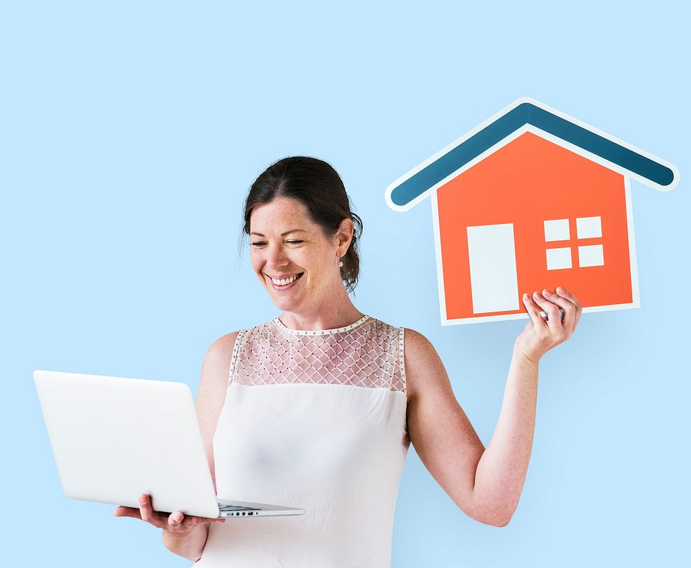 Woman holding a house icon and using a laptop