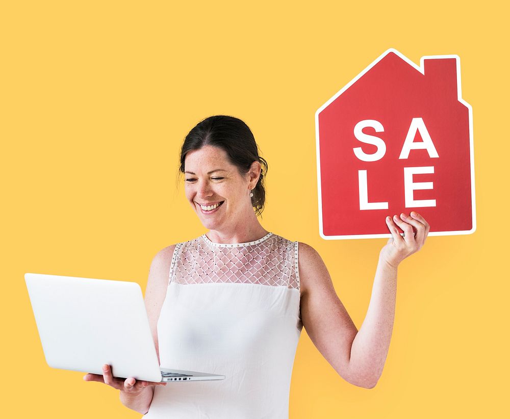 Woman holding a house sale icon and using a laptop